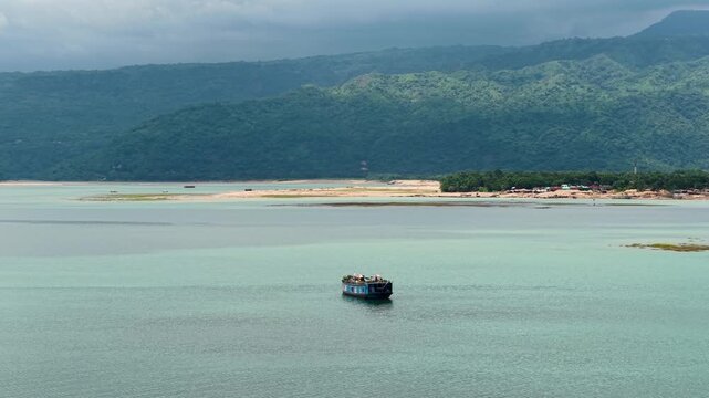 Aerial view of a boat carrying people on the waters of Tanguar Haor with lush green hills in the background, Sunamganj District, Sylhet Division, Bangladesh.
