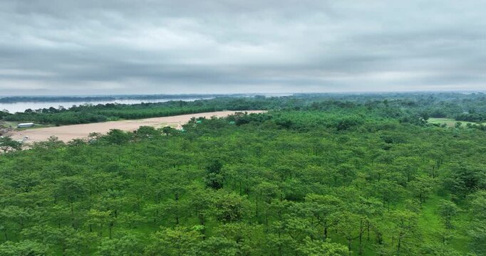 Aerial view of Tanguar Haor wetland featuring dense green trees along the riverbank under an overcast sky in Sunamganj District, Sylhet Division, Bangladesh.