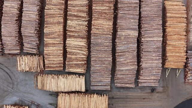 Massive timber yard with rows of stacked lumber planks and log bundles arranged in parallel patterns on industrial port surface. Washington State, USA. Aerial top down rising shot. Cloudy day.