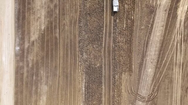Top down aerial view of heavy earthworks and soil grading for new industrial or data center development with construction vehicle moving across prepared terrain drone shot
