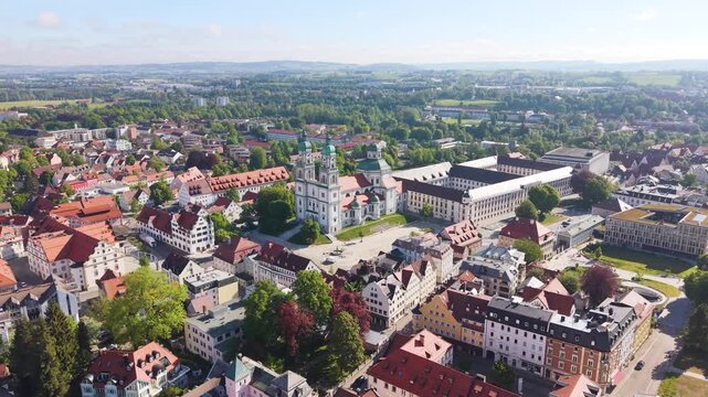 Aerial panorama of Kempten in Bavaria featuring the Basilica of Saint Lorenz surrounded by historic buildings and a green urban landscape under bright daylight, UHD.