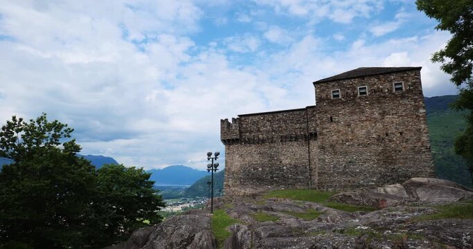 Bellinzona, Switzerland, May 18, 2026. Wide panning shot of the historic medieval Castello di Sasso Corbaro fortifications built on a rocky hill against mountain peaks and a cloudy sky
