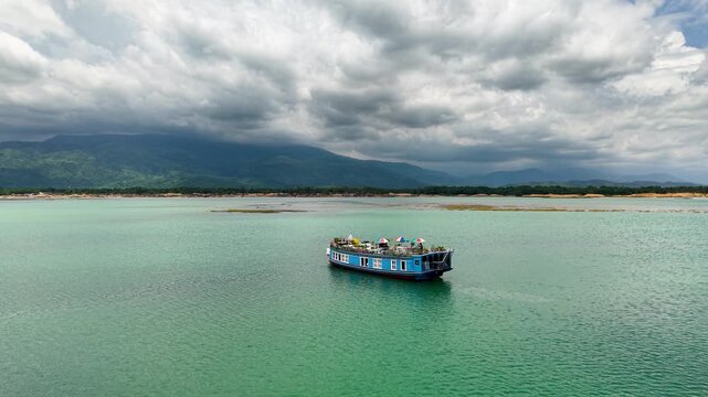 Aerial view of a blue houseboat on the turquoise waters of Tanguar Haor with hills in the background, Sunamganj District, Sylhet Division, Bangladesh.