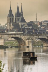 Obraz premium Golden morning light bathes the ancient church with towering spires, reflecting off the calm river. A solitary boat gently navigates, creating ripples in the peaceful waters