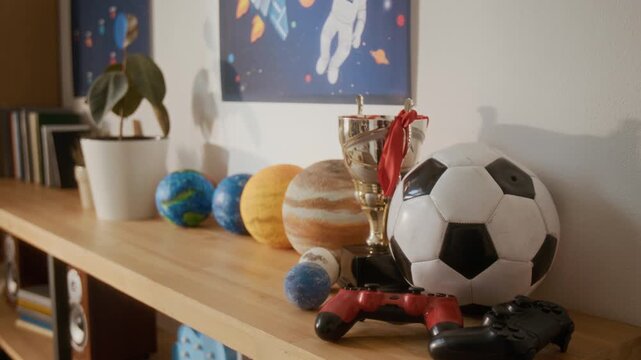 Toys, soccer ball, trophy, and game controllers sitting on wooden shelf in teenager bedroom. Video suitable for youth lifestyle, gaming, or parenting commercials
