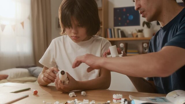Young adult man and multiethnic boy assembling toy space rocket model together at table. Footage is ideal for promoting STEM education and family bonding in toy store commercials