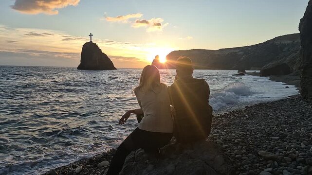 Couple, sunset, ocean Sitting together watching the majestic sunset over the sea stack and rugged coastline Vertical video