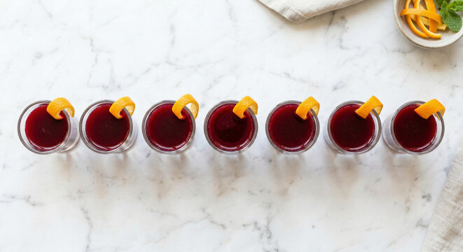 Beet kvass shots with orange peel on white marble