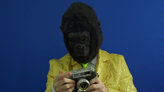 Funny character wearing a gorilla mask and a shiny jacket taking pictures with a vintage camera