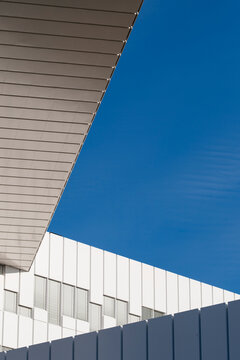 Sharp roof edge cuts across blue sky beside a modern office building where abstract architecture forms clean facade lines and open urban space