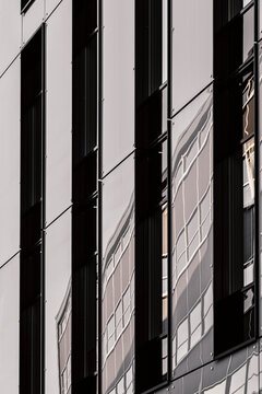 Dark window lines cross a modern office building where abstract architecture turns the facade into vertical panels, reflection, and hard urban shadow