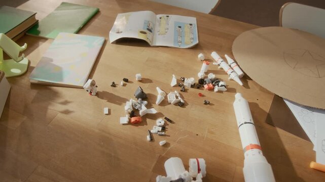Close-up shot of toy rocket parts, markers, and astronaut drawings lying on wooden table during creative science project. Clip serves well for promoting STEM education programs and creative workshops