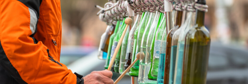 Street musician performing with glass bottles as instruments, showcasing creativity, urban street culture, improvisation, and live public entertainment in a city environment.