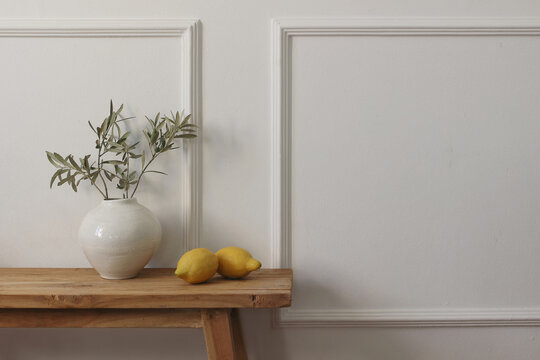 Elegant living room still life. Lemons fruit, olive tree branches in vase on wooden table, bench. Natural light, neutral tones, empty copy space. Elegant interior. Modern Mediterranean home styling.
