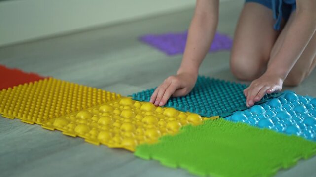 A child sits on the floor assembling colorful rubber foot massage mats, boosting fine motor skills and preventing pediatric flat feet. Occupational therapy ads, Montessori activity guides, podiatry