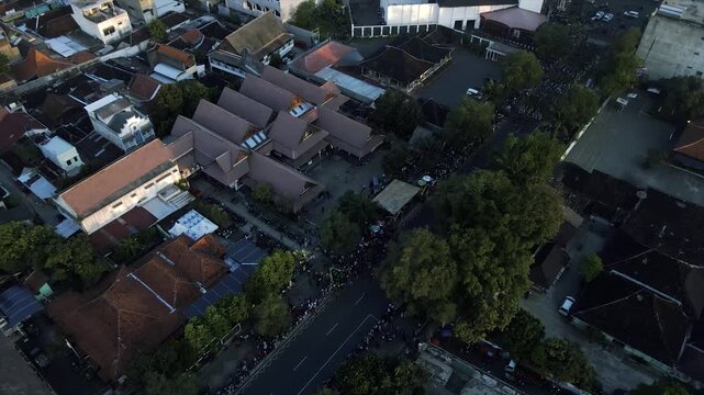 Aerial 4K Yogyakarta, odong-odong parade at twilight, vibrant LED floats, dense crowds, classic Javanese roofs, heritage town.