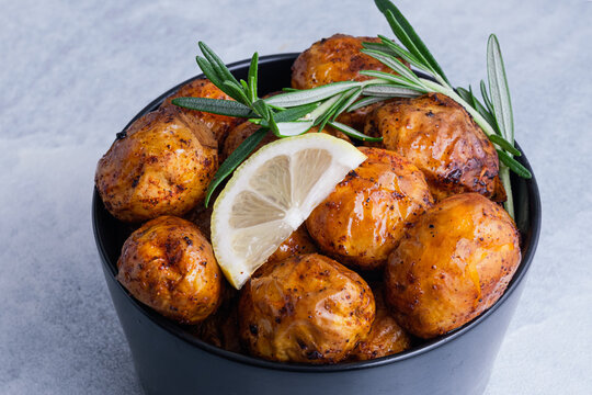 A bowl holds roasted crispy potatoes garnished with lemon slices and fresh rosemary on a blue background. Homemade comfort food and healthy side dishes. top view