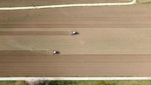 Aerial view of two tractors tilling a large agricultural field with parallel soil lines in Tubingen, Baden-Wurttemberg, Germany.
