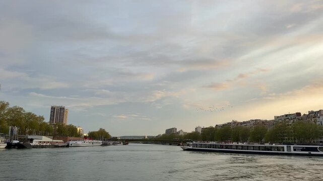 Beautiful Parisian cityscape with a touristic bateau mouche sailing on the Seine river and people walking on the riverfront at sunset, a popular and romantic destination for traveling in Europe