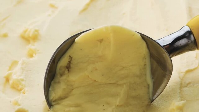 4K Video of a professional metal scoop rolling a perfect ball of creamy vanilla bean ice cream with specks, creating a smooth texture in a tub, ideal for sweet summer dessert commercials and food mark
