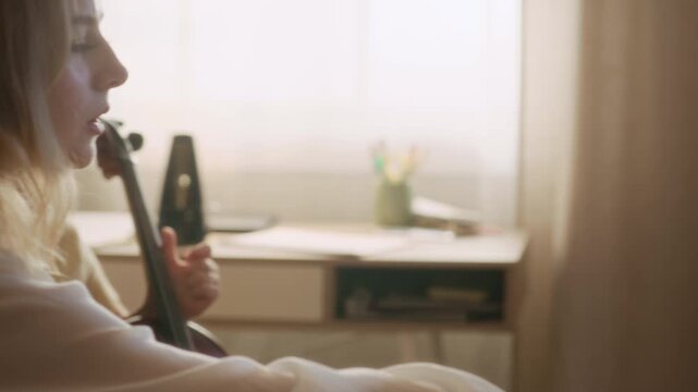 Handheld shot of young Caucasian female teacher playing violin and instructing child girl playing cello during home lesson. Clip is perfect for promoting music schools and tutoring services