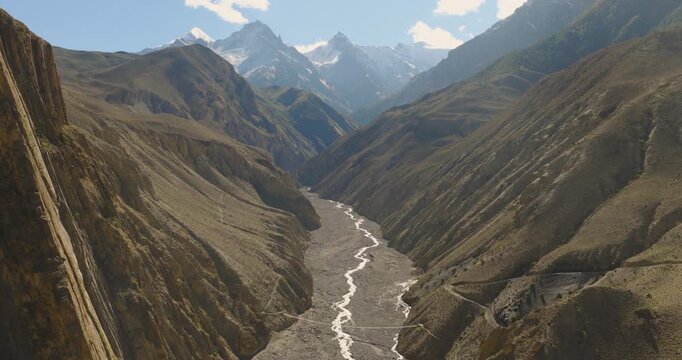 Drone tilts upward to reveal a sweeping, rugged valley and winding river carved deep into the mountain landscape of Mustang, Nepal.