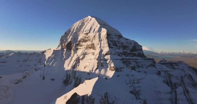 A slow lateral drone glide shot focuses on the snow-covered summit of Mount Kailash, Tibet, capturing detailed rocky ridges, mountain textures, and the upper peak against a bright, clear sky.