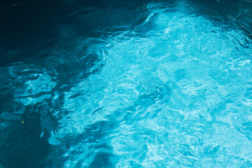 Obraz na płótnie Canvas Top view of crystal clear blue swimming pool water texture with gentle ripples and sunlight reflections for summer background.