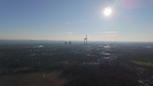 In Nowa Huta in Krak&oacute;w, residential apartment blocks and nearby industrial facilities with smokestacks rise above green spaces under a clear daytime sky in a drone cityscape view.