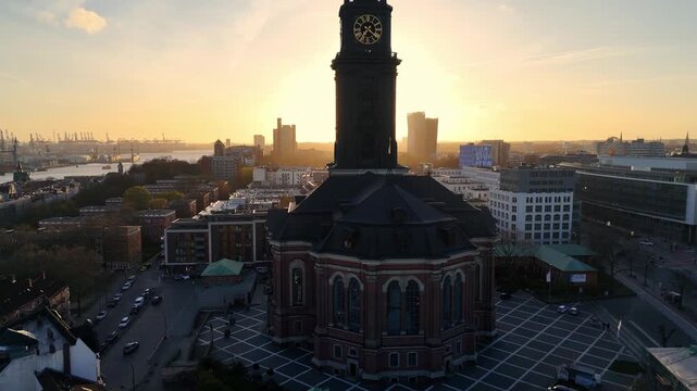 Aerial view of St. Michaeliskirche with its iconic clock tower silhouetted against the golden sunset over the city skyline in Hamburg, Hamburg, Germany.