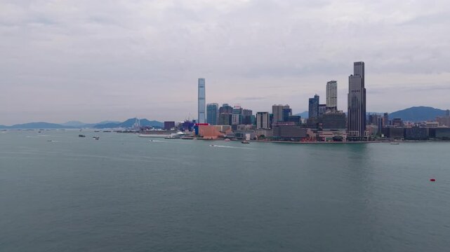 Aerial flyover over Victoria Harbour with ferries and boats toward Tsim Sha Tsui skyline ICC tower and Kowloon waterfront in Hong Kong