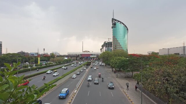 Evening traffic on Raghvendra Marg near Cybercity metro station and DLF Gateway Tower in Gurgaon, India, modern business district with urban development and construction skyline.