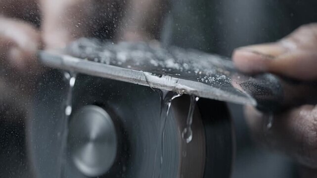 Focused view of a wet grinding process on a knife edge with water cooling the blade as the artisan refines the blades sharpness and shape