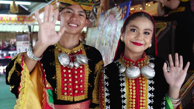 Young man and girl waving and smiling with complete set of Dusun Tindal Clothes Sinipak during Harvest Festival in Sabah