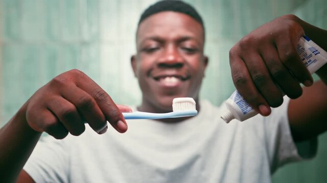 Smiling Young Black Man Prepares His Toothbrush With Toothpaste for Daily Oral Hygiene