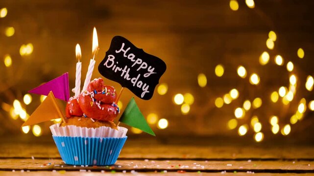 4K Video of lighting and blowing out candles on a festive birthday cupcake with red frosting, a Happy Birthday sign, and colorful flags against a warm bokeh background, perfect for celebration