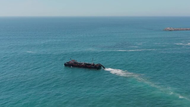 Dredger works in the sea. Aerial view to the working dredger ship in the ocean on sunny day.  A marine vessel washes sand. A sea ship deepens the coastal ocean floor.
