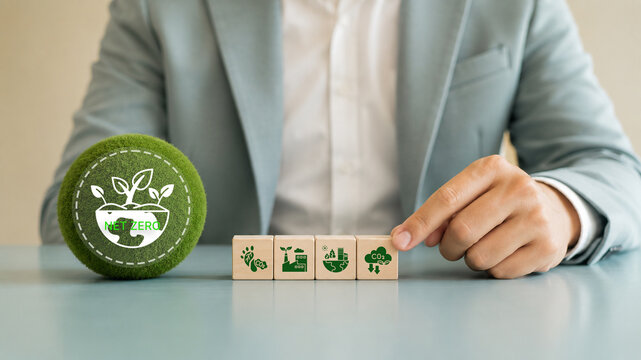 Net Zero, sustainable business strategy concept. Hand arranging wooden blocks with sustainability icons with green sphere labeled "Net Zero". Corporate commitment to environmental responsibility.