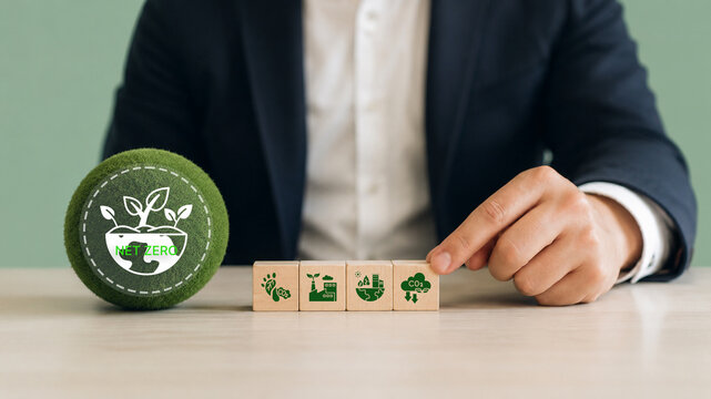 Net Zero, sustainable business strategy concept. Hand arranging wooden blocks with sustainability icons with green sphere labeled "Net Zero". Corporate commitment to environmental responsibility.