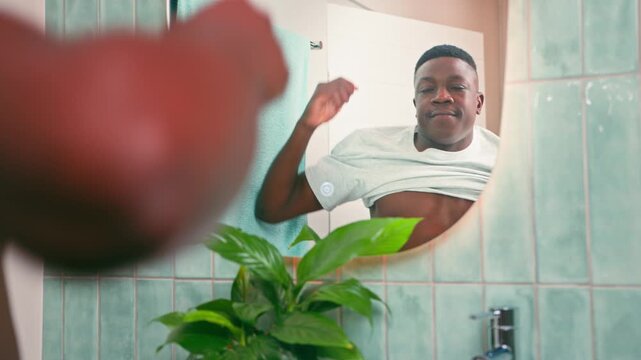 Confident Black Man Puts On A Fresh White T-Shirt In The Bathroom Mirror During Morning Routine