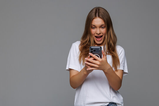 Young woman shocked by mobile phone news or message isolated on gray background