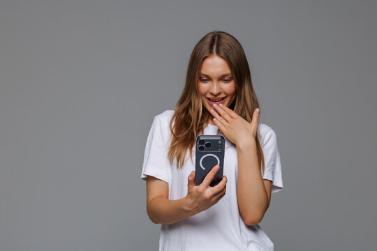 Young woman shocked by mobile phone news or message isolated on gray background