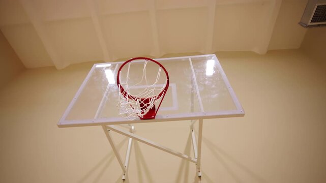 Basketball rim with mesh on transparent plastic shield in gym low angle shot. Team ball game equipment in lit gymnasium of school building
