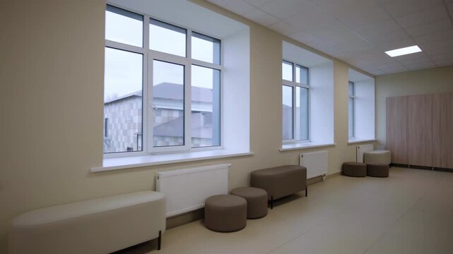 Cozy poufs near large windows in empty school corridor interior. Soft seats for children rest at breaks between lessons in building