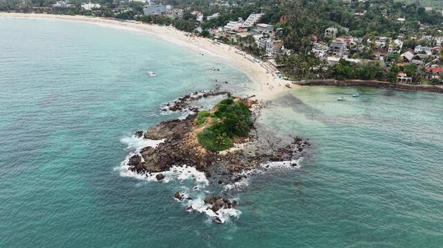 Aerial view of Parrot Rock surrounded by turquoise ocean waves and a sandy beach in Mirissa, Southern Province, Sri Lanka.