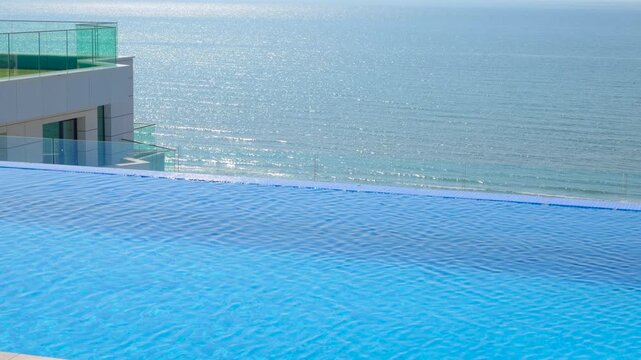 Rooftop infinity pool overlooking the glistening ocean. Luxurious rooftop infinity pool with crystal clear blue water rippling in the wind, overlooking a stunning panoramic view of the sparkling sea