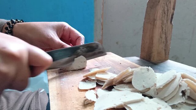 Slicing raw meatball with a knife on a wooden board for traditional Indonesian snack preparation