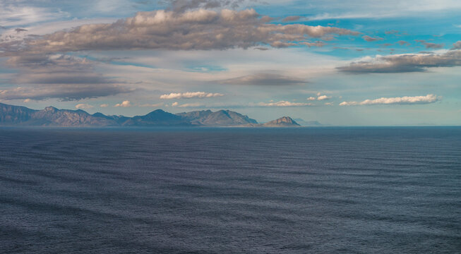 Wide seascape with textured ocean, serrated coastal mountains, and layered clouds near Cape Town, looking toward the Cape of Good Hope in soft late day light.
