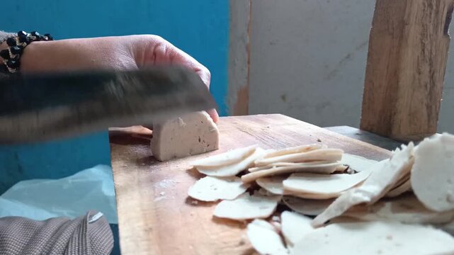 Slicing meatball thin layers on a wooden chopping board for making crispy basreng snack