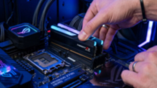 Soft focus blurred photo of Person installing new ram memory module into a computer motherboard inside a pc gaming case with blue neon lighting for high performance hardware upgrade